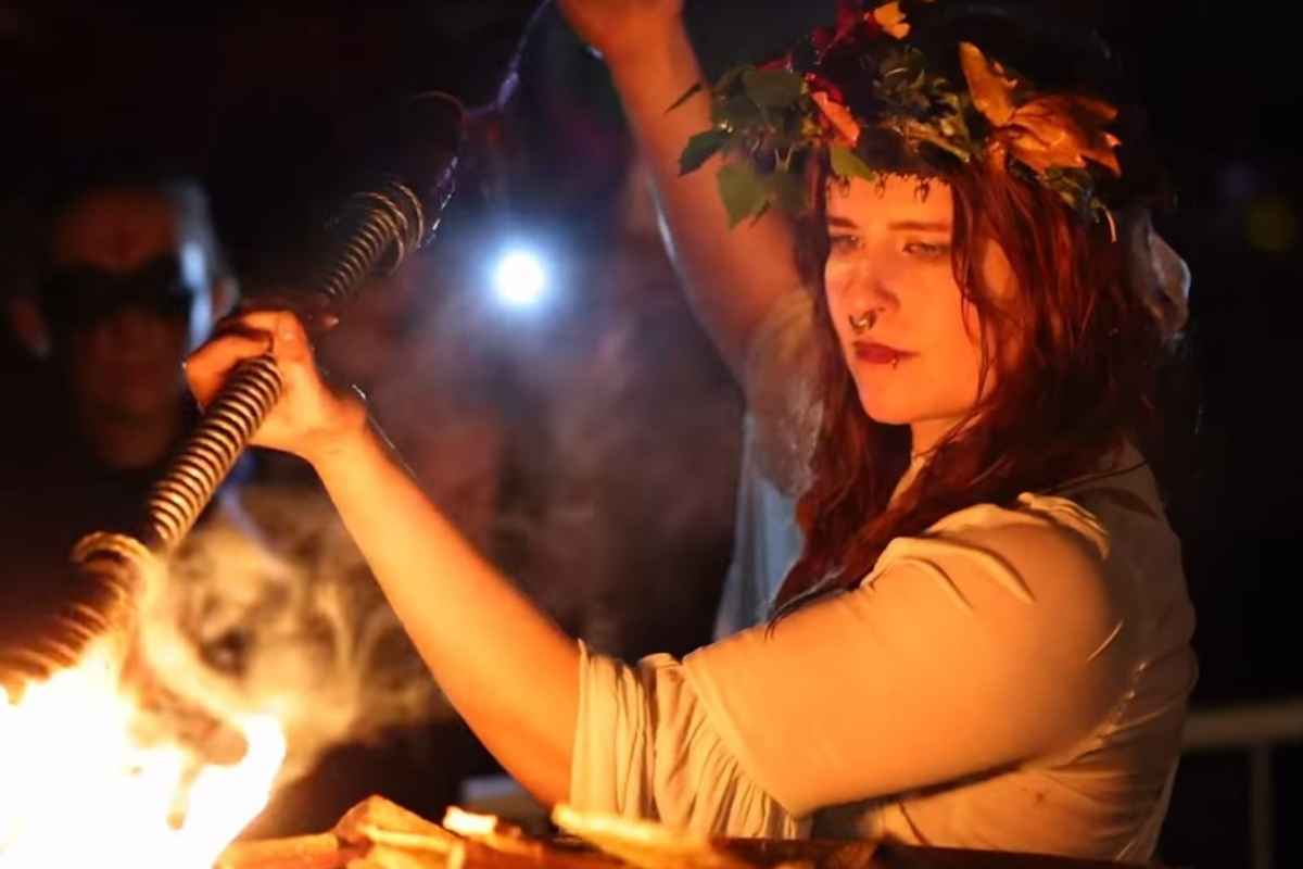 A close-up of a woman wearing a flower crown holding a flaming torch over a bonfire during the opening ceremony of the Púca Festival in County Meath, Ireland.